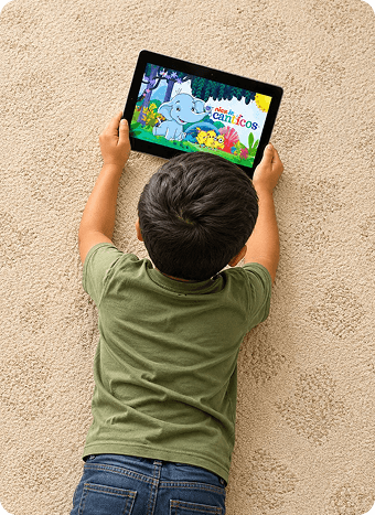 A child lying on a carpet playing on a tablet