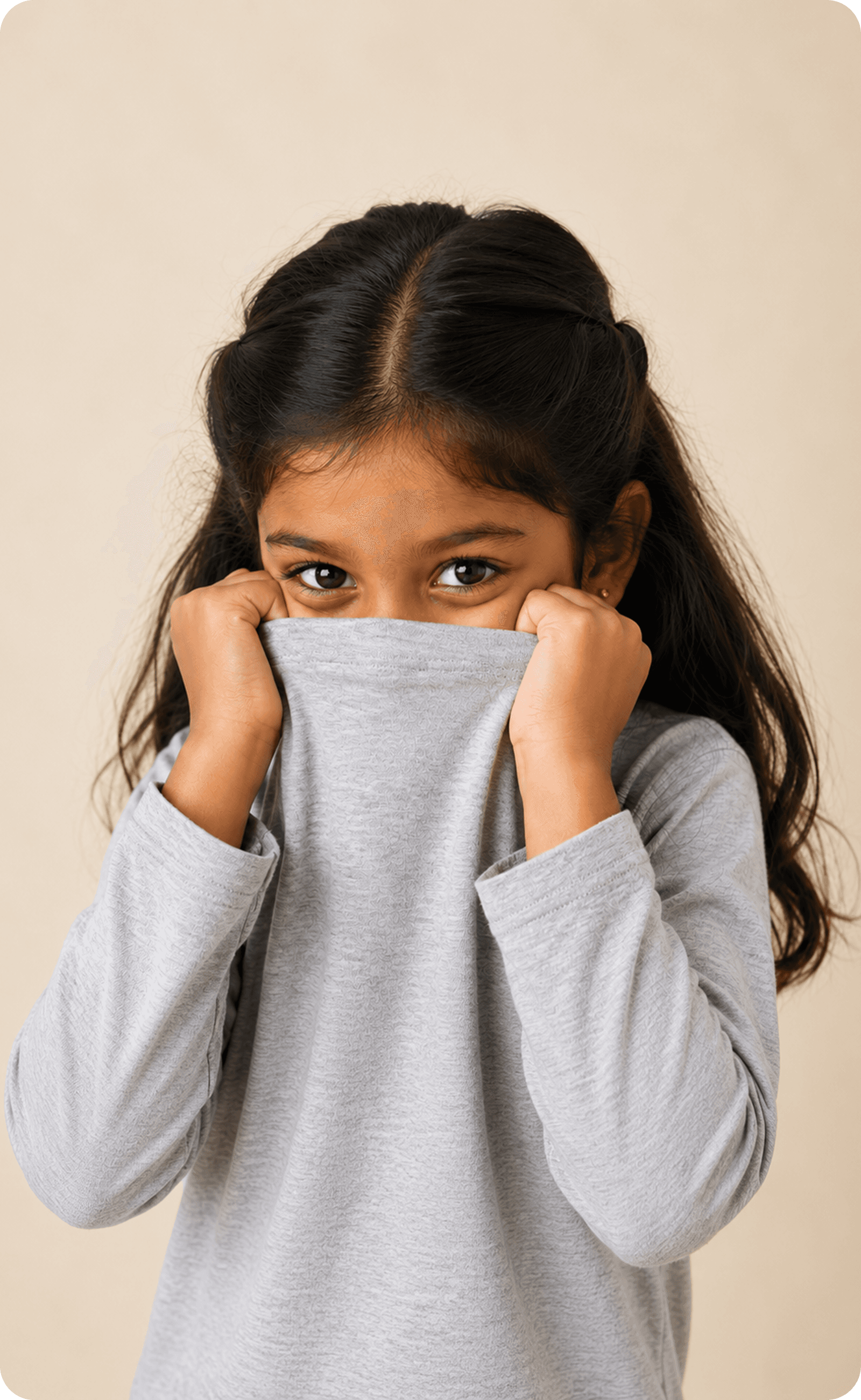 A girl pulling her jumper up over the lower half of her face, looking at the camera