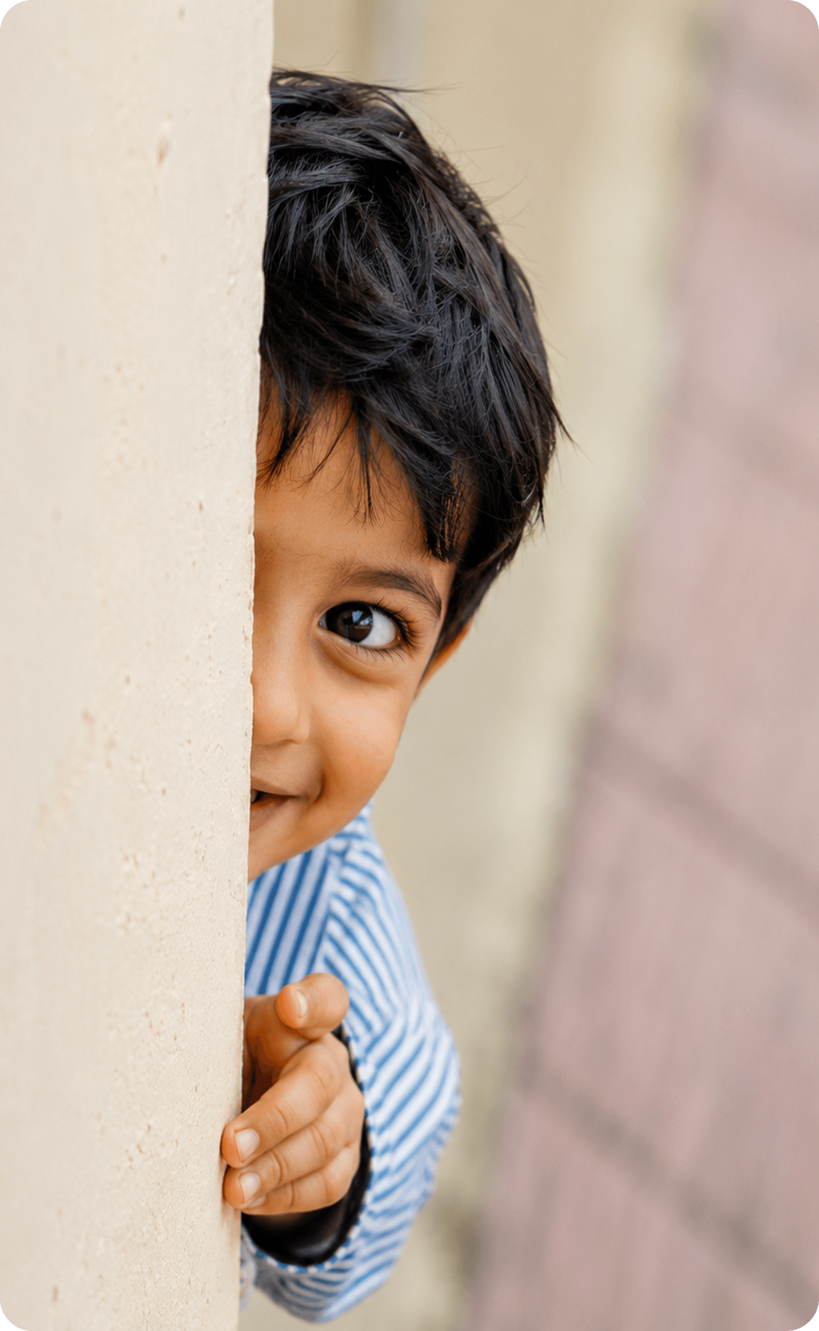 A boy peeking out from behind a wall, smiling