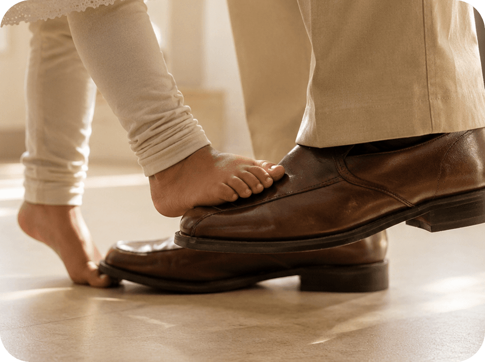 A child standing barefoot on her father's shoes