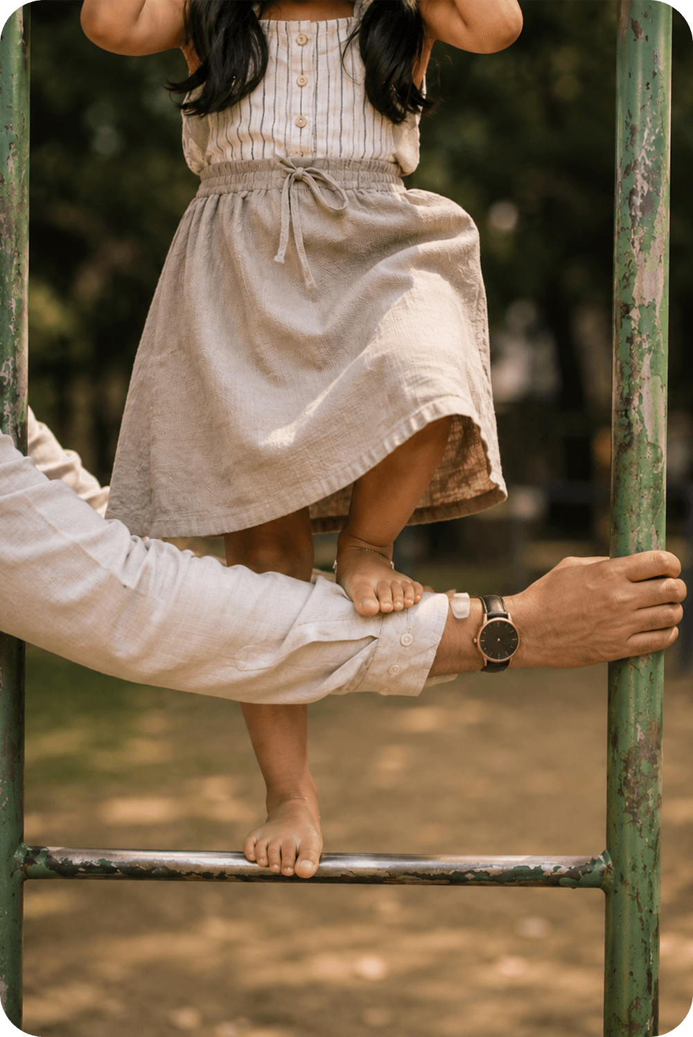 A girl walking a low balance beam, steadied by a parent's hands